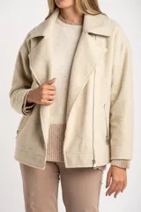 Campera de abrigo color crema, con cuello solapa y cierre asimétrico frontal. Presenta textura bouclé o de lana rizada.