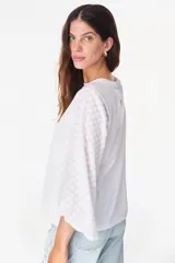 Blusa blanca de algodón, de corte recto y cuello redondo, con mangas largas abullonadas semitransparentes con textura calada de pequeñas flores y puños elásticos.