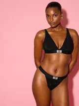 Bralette negro sin forro y sin aro, con escote en V profundo y silueta triangular. Cuenta con tirantes ajustables, detalles de cristales en toda la prenda y un parche brillante con logotipo de diamantes de imitación en la banda inferior.
