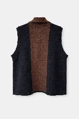 Chaleco abierto de lana, con diseño de bloques de color verticales en tonos marrón, gris y negro. Presenta un detalle de bordado artesanal con tres líneas horizontales en el frente y un ajuste holgado.