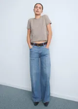 Pantalón jeans de tiro alto y corte wide leg, confeccionado en tejido de algodón con elasticidad. Presenta diseño de cinco bolsillos, cierre frontal con botón y cremallera, y trabillas para cinturón.