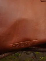 Cartera de cuero mediana con manijas largas, diseño con borde superior en corte en V y terminación artesanal con costuras contrastantes.