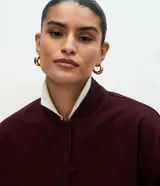 Campera estilo bomber de sarga color bordó, con cuello alto, cierre frontal con botones forrados, mangas largas con puños elásticos y bajo ajustado.