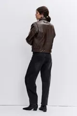 Cazadora de efecto piel en color marrón chocolate, con cuello clásico, cierre frontal con cremallera, bolsillos laterales y puños con botón.