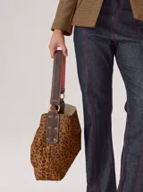 Cartera tipo hobo de cuero azul con textura granulada. Presenta un diseño holgado, con una correa de hombro bicolor que combina azul y rojo, sujeta por argollas metálicas. Incluye una placa metálica pequeña con el logo de la marca en la parte inferior frontal.