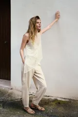 Top sin mangas de cuello redondo, confeccionado en tejido cubierto de lentejuelas brillantes. Presenta un diseño asimétrico en el bajo con una caída lateral pronunciada y cuenta con un forro interior con tirantes finos. Incluye cierre en la espalda con abertura y botón oculto.