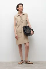 Vestido corto color beige, sin mangas, con cuello camisero, cierre frontal con cordones cruzados y múltiples bolsillos con cierre.