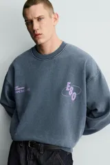 Sudadera de corte boxy fit con efecto lavado, cuello redondo y manga larga. Presenta estampados a contraste en color violeta en la parte frontal y acabados en rib en cuello, puños y ruedo.