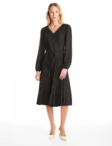 Vestido midi negro de seda fría con escote en V decorado con aplique de guipur y lazo central. Presenta mangas largas fluidas con puños fruncidos, hombros con leves frunces y cintura ajustable con lazo que da paso a una falda plisada.