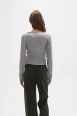 Sweater de punto gris con cuello en V, diseño cruzado y cierre lateral con botones. Presenta mangas largas y un ajuste al cuerpo con detalle acanalado en la cintura.