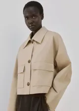 Chaqueta corta de algodón en color beige, con cuello camisero, mangas largas, dos bolsillos con solapa en el frente y cierre de botones.
