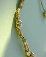 Collar artesanal compuesto por piezas metálicas irregulares con acabado dorado, ensartadas en un cordón de hilo de algodón natural. Presenta un sistema de nudo corredizo para ajustar el largo.