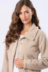 Campera de sherpa color beige, con cuello camisero, cierre frontal con botones a presión y detalles de ribete en la solapa y puños.