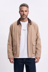 Campera color taupe con cuello de pana marrón oscuro, cierre frontal y botones a presión. Cuenta con dos bolsillos frontales con solapa.