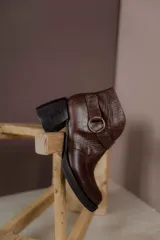 Bota corta de cuero vacuno con textura de reptil, color marrón oscuro. Cuenta con un taco cuadrado negro, suela de plataforma y una tira decorativa con hebilla metálica circular en el tobillo.