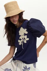 Blusa azul marino de algodón, con mangas abullonadas cortas de tela plana y gran bordado de rosa en tono crudo en el pecho.
