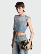 Top de denim celeste con diseño acolchado en patrón de rombos, de corte crop y sin mangas. Presenta un diseño de doble botonadura con botones dorados grabados, cuello redondo y detalles de charreteras en los hombros.