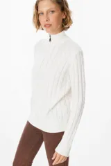 Sweater de punto gris con textura de ochos, cuello alto con cierre frontal parcial, manga larga y puños y ruedo acanalados.