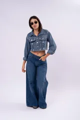 Campera de jean cropped con tachas plateadas distribuidas en el frente, hombros y mangas. Presenta un diseño con bordes deshilachados, cuello clásico y cierre frontal con botones metálicos.