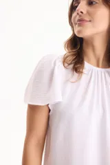 Blusa de manga corta con pliegues en escote redondo, confeccionada en tela crepé de color beige.