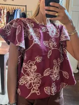 Camisa color bordó con estampado floral bordado en blanco, escote redondo y mangas cortas con volados.