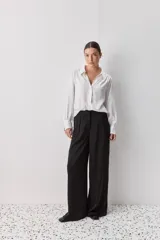 Pantalón de tiro medio, con calce amplio y piernas wide leg, color negro. Presenta pinzas delanteras, cierre frontal y bolsillos laterales funcionales.