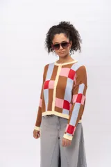 Saco tipo cardigan de tejido de punto con diseño geométrico de cuadros en tonos marrón, celeste, rosa y rojo. Presenta cuello redondo, cierre frontal con botones y terminaciones en color crema.