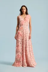 Vestido largo de encaje color rosado, con escote en V y aplicaciones de flores de tela tridimensionales en cascada sobre el hombro y el lateral de la falda. Incluye un cinturón delgado integrado en la misma tela.