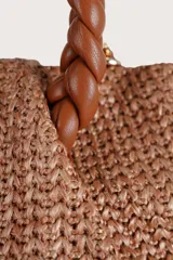 Bolso tipo mini shopper de textura tejida en color café, con asas superiores trenzadas en cuero sintético marrón y correa de cadena metálica. Incluye un detalle de etiqueta colgante de cuero sintético.