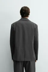 Blazer oversized fit de hombre, color gris oscuro con rayas verticales finas. Cuello con solapas de muesca, manga larga con puño abotonado, bolsillos de solapa en la cadera y bolsillo interior. Cierre frontal de un botón y abertura en el centro de la espalda.