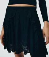 Pollera corta de encaje floral color negro, de talle alto y corte evasé, con volados y paneles superpuestos en el frente.
