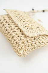 Cartera bandolera de tejido artesanal en color beige, con solapa frontal y correa larga ajustable decorada con cuentas de madera. Incluye detalles de flecos laterales con cuentas.