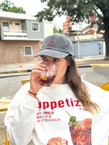 Gorro de béisbol de color gris oscuro (obsidian) con efecto lavado, confeccionado en algodón. Presenta un bordado frontal de un ají picante rojo y verde.