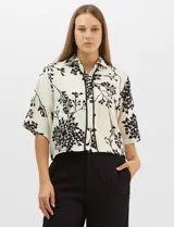 Camisa de corte holgado con estampado botánico en blanco y negro. Presenta cuello camisero, mangas cortas amplias y cierre frontal con botones y vivos a contratono.