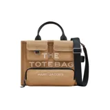 Bolso tipo tote bag Marc Jacobs modelo The Cargo Canvas Medium Tote Bag, de lona color tostado con detalles en negro. Cuenta con múltiples bolsillos frontales, asas superiores de cuero y correa de hombro ajustable y extraíble. Presenta la inscripción "THE TOTE BAG" y el logo de la marca bordados en el frente.