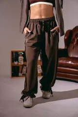 Pantalón de estilo urbano color marrón, con cintura elástica ajustable mediante cordón, bolsillos laterales y bajos ajustables con tiras. Presenta un pequeño estampado en la pierna.