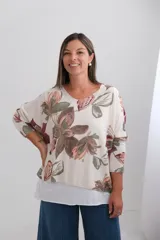Sweter de corte amplio con diseño de doble capa, escote en V y mangas largas. Presenta un estampado floral en tonos tierra sobre fondo beige, con un borde inferior en color liso que simula una segunda prenda.