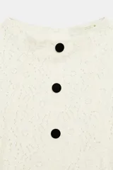 Vestido corto blanco de encaje, con cuello redondo, manga corta y bajo evasé con frunces. Cuenta con fila de falsos botones negros delanteros a contraste y cierre trasero con cremallera oculta.