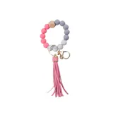 Llavero con pulsera de cuentas redondas de silicona en tonos rosa, gris y blanco, con un cubo de madera natural y borla decorativa rosa.