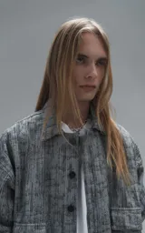 Campera de denim rígido con diseño de trama texturizada en tonos grises y negros. Presenta cuello camisero, cierre frontal con botones, mangas largas y dos bolsillos frontales con solapa.