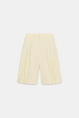 Bermudas de tiro medio color amarillo claro, confeccionadas en mezcla de algodón. Presentan cintura con trabillas, bolsillos laterales ocultos en costura, pliegues delanteros y cierre frontal con cremallera, botón y ganchos metálicos.
