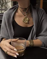 Collar con dije grande de bronce con forma orgánica y textura rugosa, suspendido de un cordón negro. Incluye cordones intercambiables.