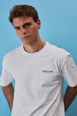 Remera blanca de algodón, de corte holgado y mangas cortas, con pequeño estampado azul en el pecho.