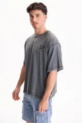 Remera oversize gris de manga corta con efecto lavado acid wash y estampa pequeña en el pecho con la palabra 'START' dentro de un recuadro amarillo.