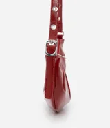 Cartera tipo shoulder bag de diseño media luna, confeccionada en poliuretano con acabado brillante. Presenta detalles frontales estilo gota, cierre superior por cremallera y correa de hombro ajustable con ojetes metálicos.