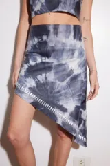 Vestido corto de cuero ovino con diseño batik en tonos de azul y blanco. Presenta tiras de cuero plateado en el escote y ruedo con detalle de ojales metálicos.