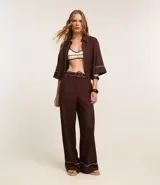Pantalón wide leg de cintura alta color marrón, confeccionado en viscolino con 15% de lino, con trabillas en la cintura y vieses contrastantes en las barras. Incluye cinturón de tejido con hebilla metalizada de efecto martillado.