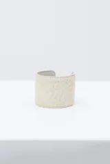 Pulsera rígida tipo brazalete de cuero en color crudo con textura efecto cocodrilo y costuras decorativas en los bordes.