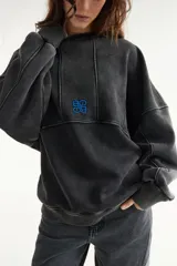 Buzo oversize de corte unisex, color rojo con efecto desgastado (acid wash), confeccionado en algodón con interior de polar. Presenta costuras frontales decorativas, hombros caídos, mangas largas con puños elastizados, rib en el cuello y el ruedo, y un pequeño logo bordado en el pecho.