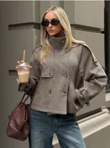 Chaqueta corta de estilo trench con estampado de cuadros pequeños, cuello alto, cierre frontal de doble botonadura y mangas con trabillas ajustables en los puños.